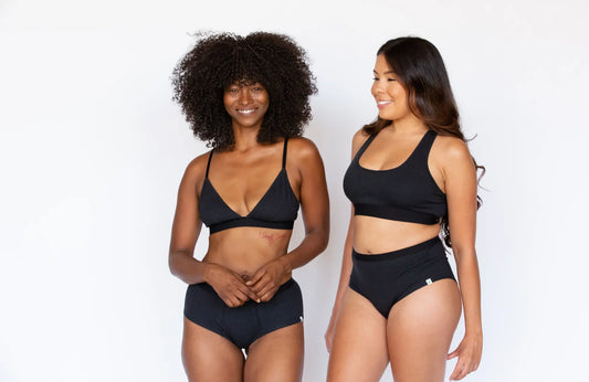  two women model black bralettes and underwear smiling against a white background.