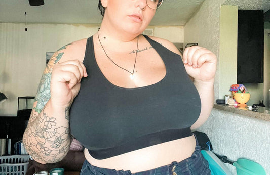 tattooed woman in glasses with short dark hair holding the side of a black racerback bralette