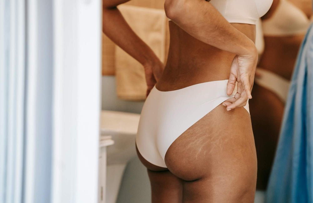A woman wearing white underwear pulls up the waistband with her hands.