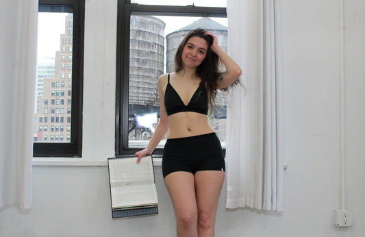 woman wearing a matching black triangle bralette and boy shorts set in front of two open windows