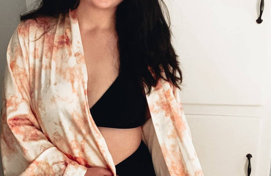 A woman with long black hair wearing a white/red robe, a black bralette, and matching underwear stands in front of a white cabinet