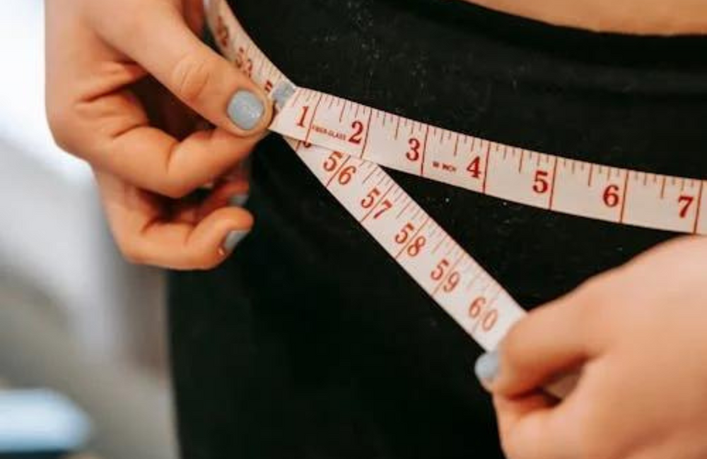 A woman with painted fingernails measures her hips with a white measuring tape.