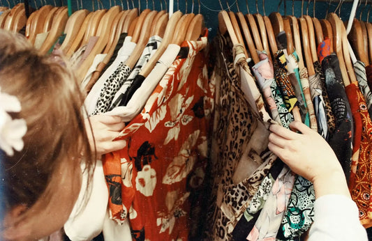 two hands searching through a rack of colorful clothing
