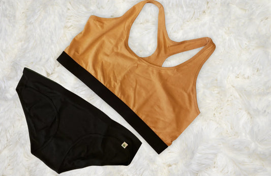 bikini underwear in black laid out flat with a light orange racerback bralette against a fuzzy white background