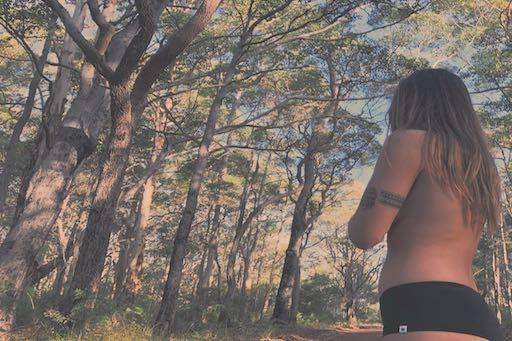 Beautiful young woman in WAMA hemp underwear in the woods, looking out at trees that risk being cut down for paper. 