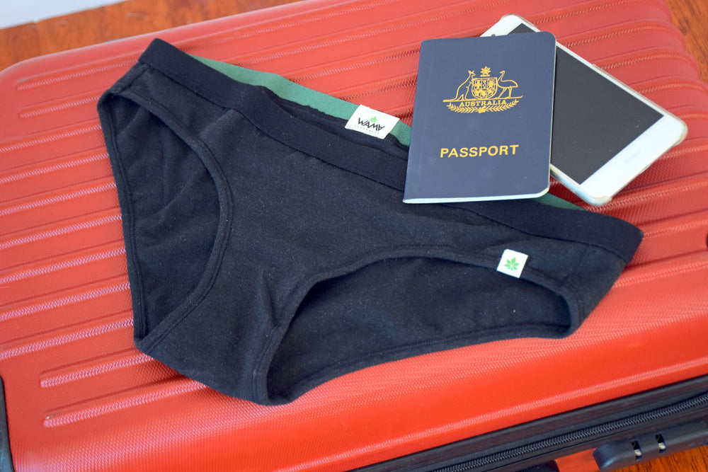 A pair of WAMA hemp travel underwear sits atop a red suitcase with a passport and cell phone.