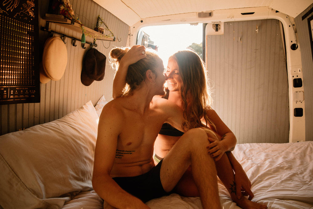 A man and a woman embrace on their van bed, both in anti chafing underwear by WAMA Underwear.