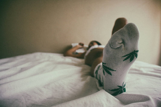 A person lays on a white bed wearing socks in a hemp leaf patterned white pair.