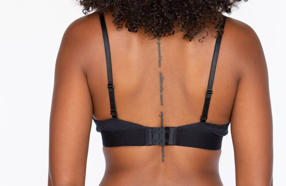 Back view of a woman with curly dark hair wearing a black bralette with a hook closure. 