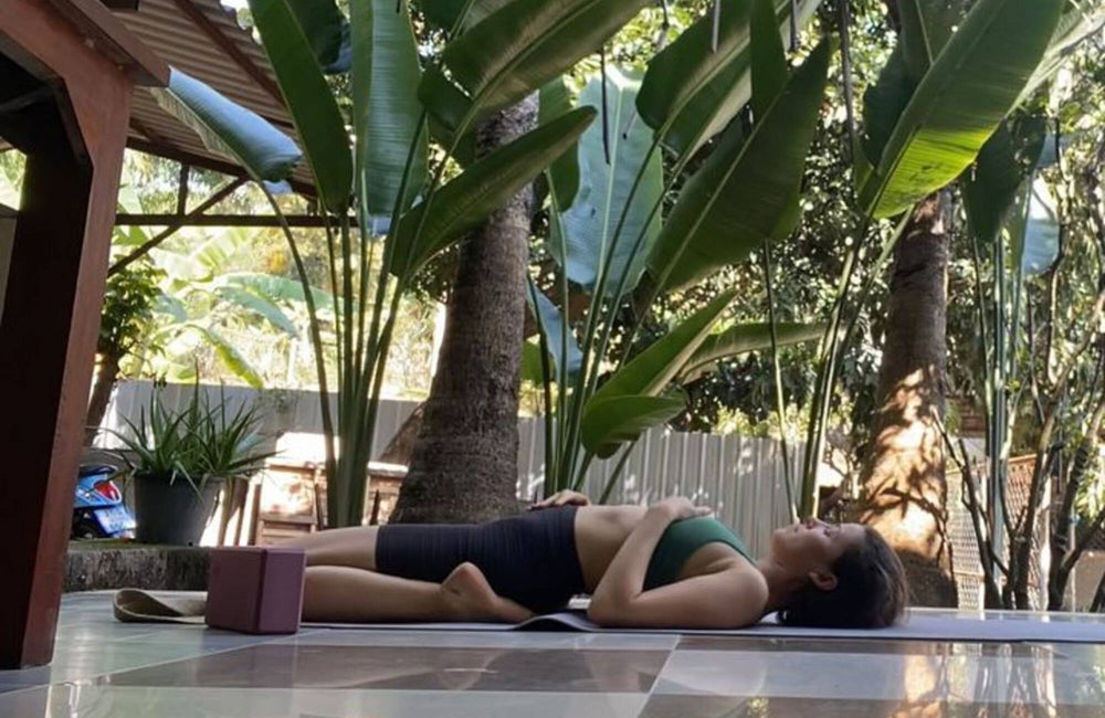 woman in a green sports bra and black bike shorts laying on her back in a yoga pose