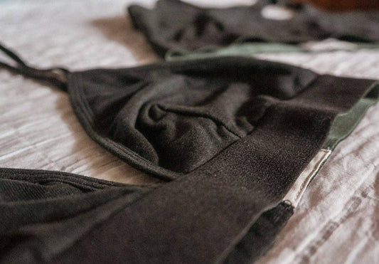 A black hemp triangle bralette, lies flat on a wrinkled linen cloth.