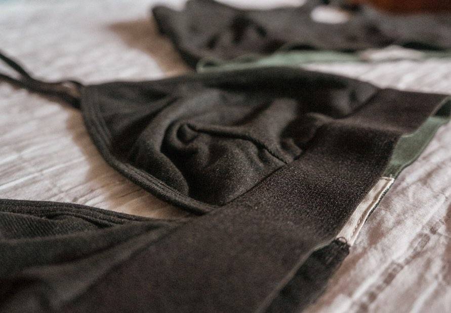 A black hemp triangle bralette, lies flat on a wrinkled linen cloth.