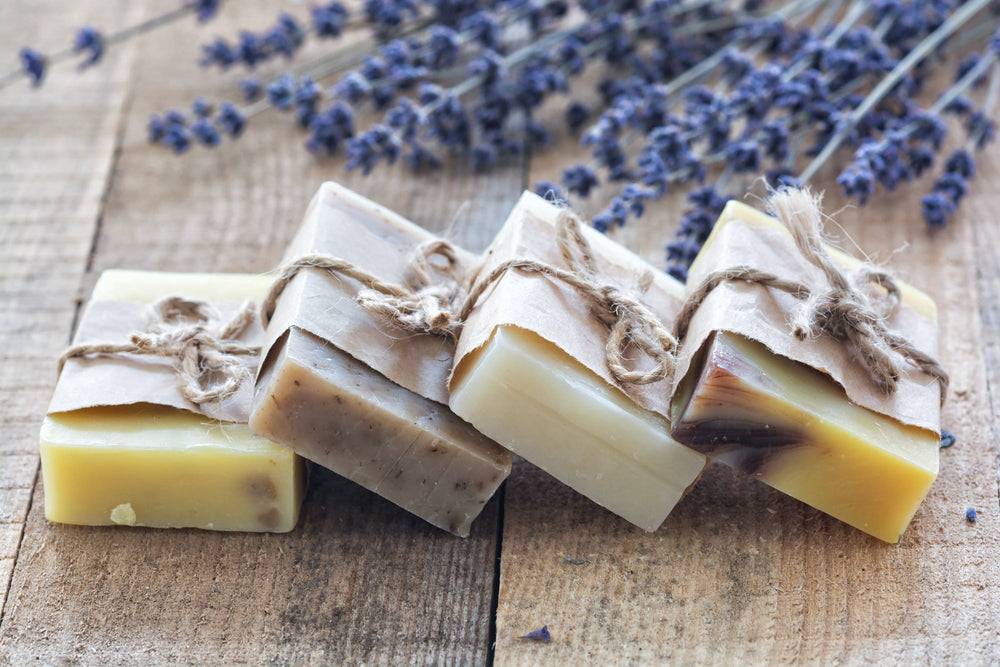 Four bars of twine and paper-wrapped hemp soap with sprigs of lavender on wooden boards.