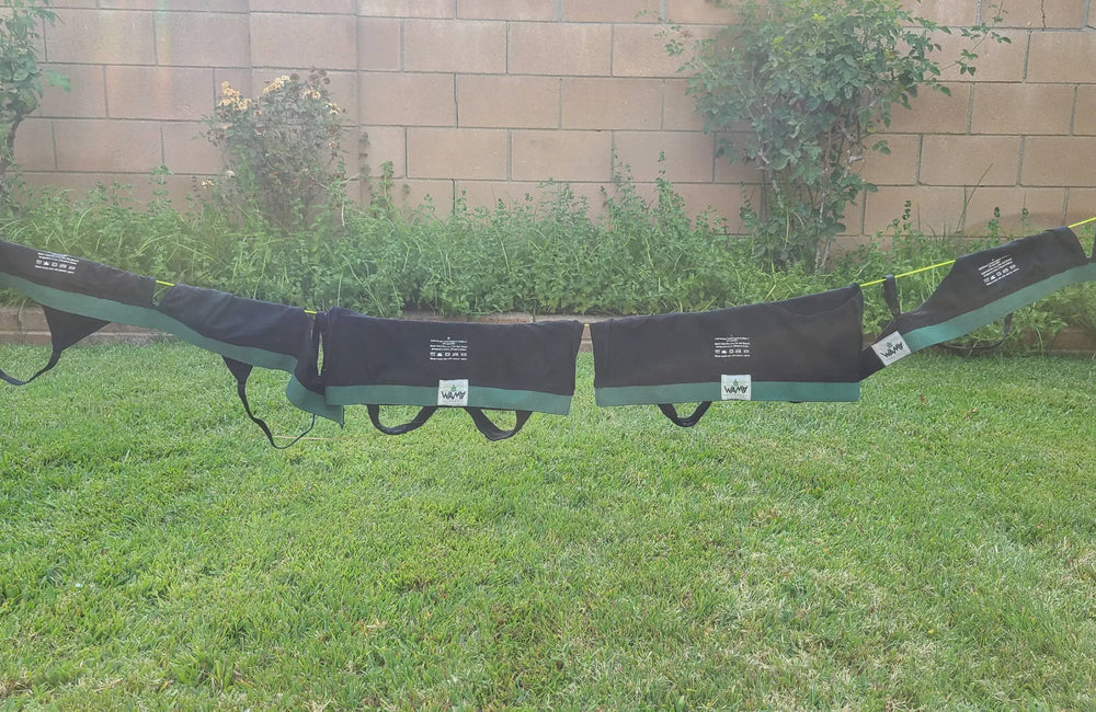 A line of black hemp bras hangs from a clothesline in a bricked-in garden, above green grass.