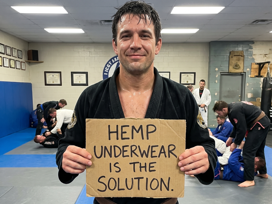 Man in a jiu-jitsu gi holding a cardboard sign reading Hemp underwear is the solution