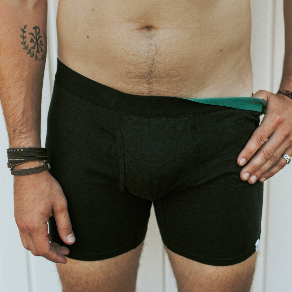 mens underwear in black color worn by a man flipping the elastic with his left hand showing the green color inside the elastic